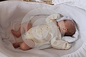 1 month old baby girl in beige bodysuit sleeps in her white cradle