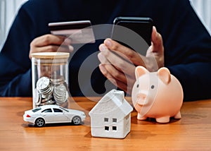 Monthly expenses, budget, financial insurance concepts. White home, car, money coin bottle and piggy bank on table while person