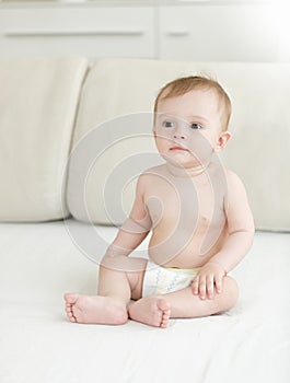 Adorable 10 months old baby boy in diapers sitting on bed