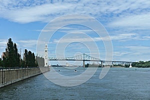 Montreal Clock Tower and Jacques Cartier Bridge at Old Port, Montreal, Canada. Background is a blue cloudy sky. Foreground is