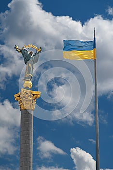 Monument of Independence in Kiev and ukrainian flag against blue sky with white clouds