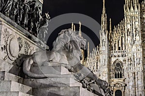 Monument of Victor Emanuelle II with Lion Statue in Milan, Italy, and Duomo Milan Cathedral in Background at Night.