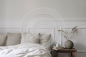 Moody boho bedroom interior. Vintage wooden bedside table. Round modern vase with dry grass. Cup of coffee on old books
