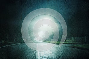 A moody concept of a straight road with street lights on a foggy night in a city. With a grunge, artistic, edit