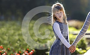 Moody cute child girl holding mother hand looking back on warm day outdoors. Family relationship and recreation