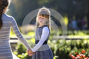 Moody cute child girl holding mother hand looking back on warm day outdoors. Family relationship and recreation