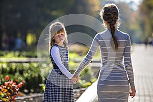 Moody cute child girl holding mother hand looking back on warm day outdoors. Family relationship and recreation