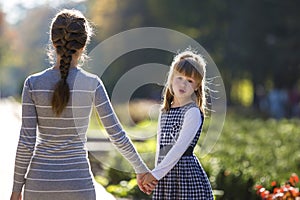 Moody cute child girl holding mother hand looking back on warm day outdoors. Family relationship and recreation