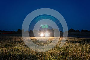 A moody edit of car headlights shining across a field on a summer`s night