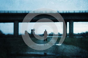 A moody figure, back to camera. Standing under a bridge in a post industrial landscape. With a grunge, abstract, edit