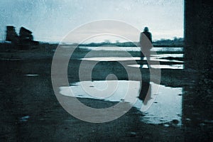 A moody figure, reflected in a puddle. Standing under a bridge in a post industrial landscape. With a grunge, abstract, edit