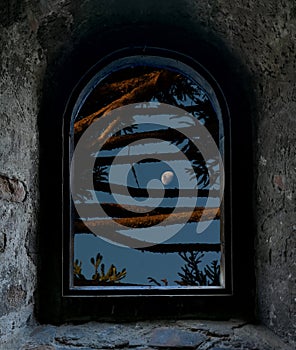 The moon in a blue sky from an old stone window