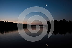 moon, in its waxing crescent, rising over peaceful lake