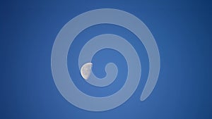 Moon moves across cloudless blue sky