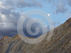 Moon over the mountain peaks at sunset in Ladakh, India.