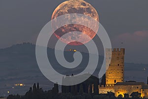 The moon over the tower of the sper dynasty in tuscany, italy. a red full eclipse is visible at the top of it