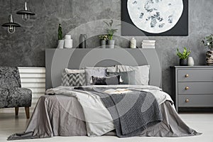 Moon poster on concrete wall above bed with bedhead in grey bedroom interior. Real photo
