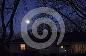 Moon rise over a house with lights on.