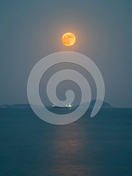 the moon rises over the ocean with large rocks in the background