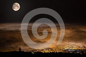 The moon is shining on the clouds. Below that is the illuminated city of Puerto de la Cruz.