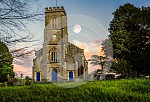 Moon in the sky at sunset behind church clock tower in Corsley, Wiltshire, UK