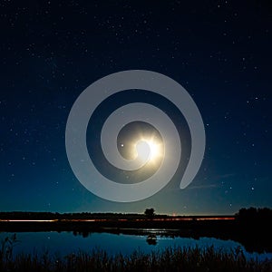 The moon and the stars in night sky reflected in the river.