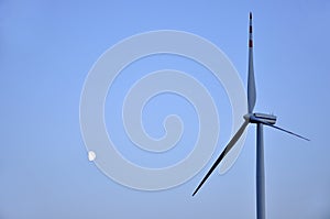 Moon and wind turbine against the blue sky