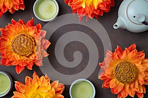 Mooncakes in orange dahlia flowers, teapot and cups of green tea on brown background. Chinese mid-autumn festival food