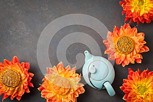 Mooncakes in orange dahlia flowers, teapot and cups of green tea on brown background. Chinese mid-autumn festival food