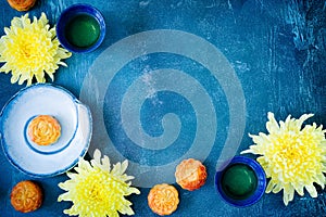 Mooncakes, tea, chrysanthemum flowers on blue background with copy space. Chinese mid-autumn festival food.