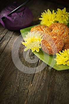 Mooncakes, teapot, yellow chrysanthemum flowers on wooden background. Chinese mid-autumn festival food