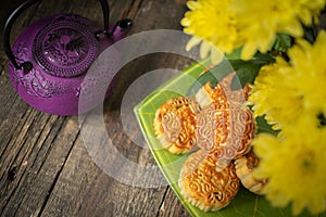 Mooncakes, teapot, yellow chrysanthemum flowers on wooden background. Chinese mid-autumn festival food