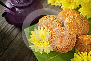 Mooncakes, teapot, yellow chrysanthemum flowers on wooden background. Chinese mid-autumn festival food