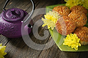 Mooncakes, teapot, yellow chrysanthemum flowers on wooden background. Chinese mid-autumn festival food
