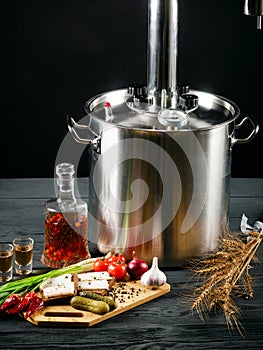 Moonshine still on a black wooden background. Alcohol in a glass decanter. Snack on the cutting board