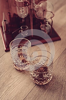 Moonshine still and two glasses with ice and whiskey on wooden background