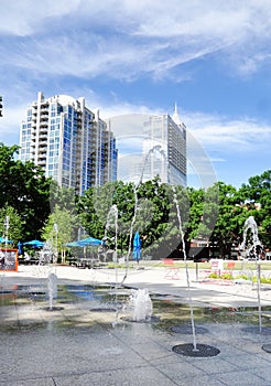 Moore Square Park with splashpad fountain and downtown Raleigh buildings in the distance