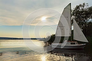 Moored boat with sail at sunset, lake.