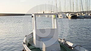 Moored fishing boat is lulled by the water while the sun reflects off the sea early in the morning