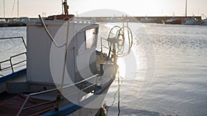 Moored fishing boat is lulled by the water while the sun reflects off the sea early in the morning