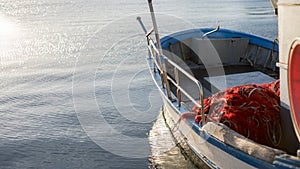 The moored fishing boat is lulled by the water while the sun reflects on the sea early in the morning with the red fishing net in
