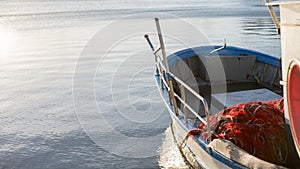 The moored fishing boat is lulled by the water while the sun reflects on the sea early in the morning with the red fishing net in