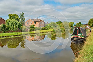 A moored houseboat on the Leeds Liverpool canal near Burscough with beautiful reflections and a swan on the water
