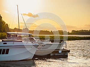 Moored pleasure boat and motorboat near the old wooden pier on the lake in the evening with sunset light on the background