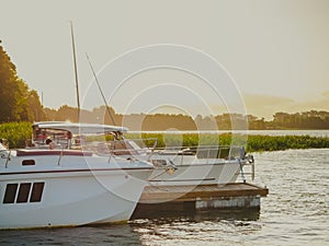 Moored pleasure boat and motorboat near the old wooden pier on the lake in the evening with sunset light on the background