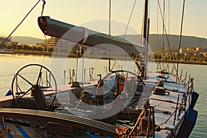 Moored yacht. From the yacht`s deck to the bow and sails. Gear and equipment on the boat. City Koper in the background