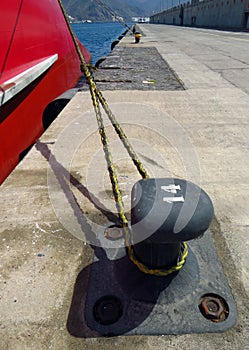 Mooring bollard with heavy duty mooring ropes. Detail of mooring with the rope of the boat in the dock. Noray with red merchant photo