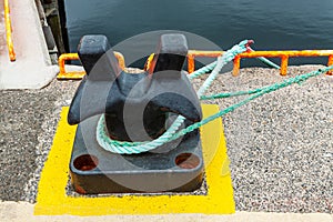 Mooring cable tied to an iron bollard on a concrete dock, boat cable