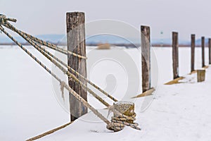 Mooring rope and bollard on lake in cold winter with snow background