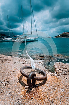 Mooring rope and bollard on sea water and yacht at the background. Dramatic Rainy clouds above mediterranean sea